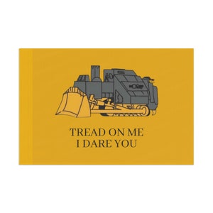 Op de afbeelding: Een gele vlag met een zwarte en grijze bulldozer-illustratie en de tekst "Tread on me I dare you".