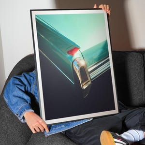 Pu&ograve; includere: Stampa incorniciata con un primo piano della parte posteriore di un'auto vintage teal. L'immagine evidenzia il fanale posteriore e i dettagli cromati dell'auto su uno sfondo teal e nero. La stampa &egrave; tenuta da una persona.