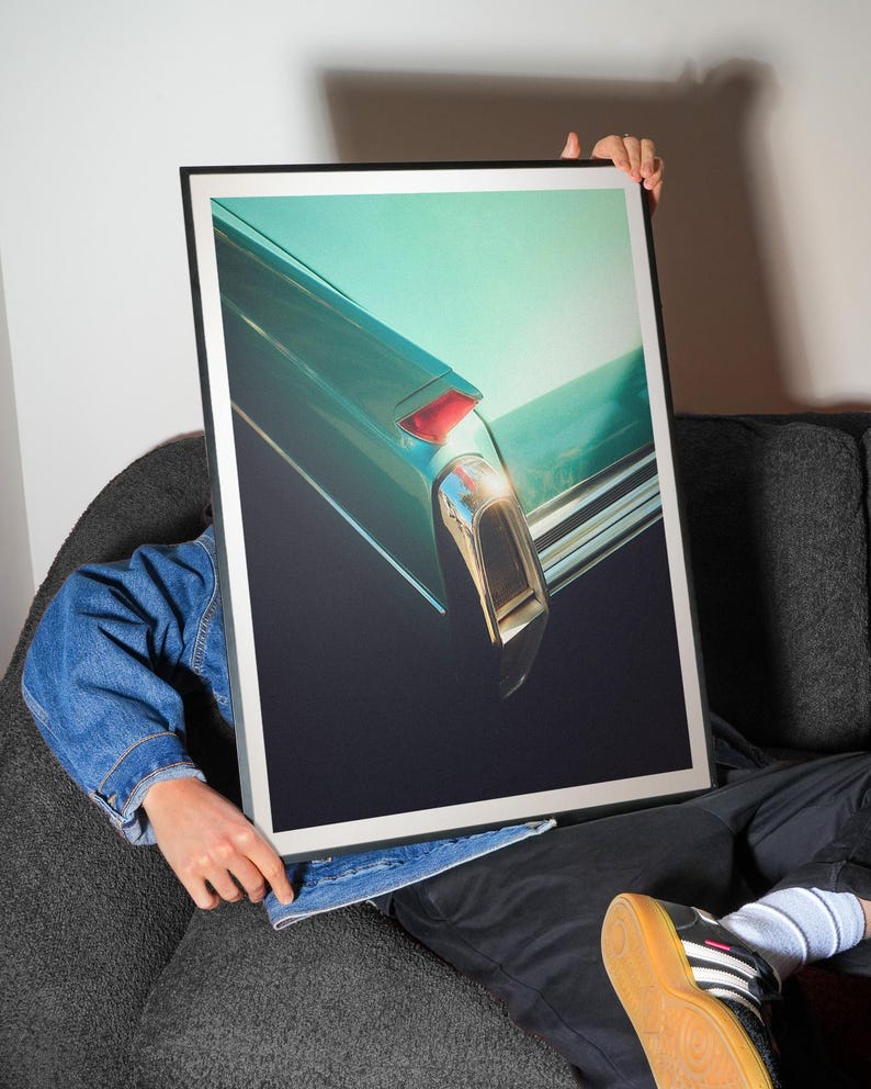 Pu&ograve; includere: Stampa incorniciata con un primo piano della parte posteriore di un'auto vintage teal. L'immagine evidenzia il fanale posteriore e i dettagli cromati dell'auto su uno sfondo teal e nero. La stampa &egrave; tenuta da una persona.