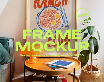 May include: A framed poster with the word "RAMEN" in orange lettering. The poster features a bowl of ramen with eggs and chopsticks. A two-tiered wooden side table holds books and a lamp. A plant in a woven basket is to the right.