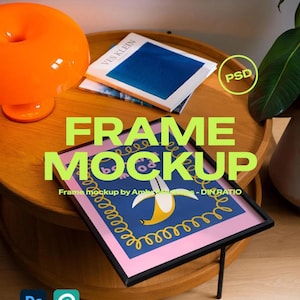 Puede incluir: Una maqueta de marco con un diseño de plátano, exhibida sobre una mesa de madera. La obra de arte presenta un marco negro, un borde rosa y un fondo azul con una ilustración de plátano amarillo. Una lámpara naranja y libros también están sobre la mesa.