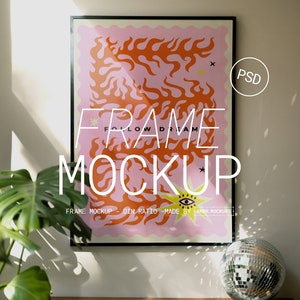 Puede incluir: Un póster enmarcado en negro con un diseño abstracto rosa y naranja. El póster tiene el texto "FRAME MOCKUP - DIN RATIO - MADE BY AMBR.MOCKUPS" en la parte inferior. El póster está colgado en una pared blanca con una bola de discoteca en primer plano.