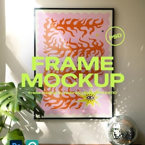 May include: A framed poster with a pink background and orange flame-like shapes. The poster has the words "FRAME MOCKUP" in large, neon green letters. A disco ball sits on a wooden surface below the poster.