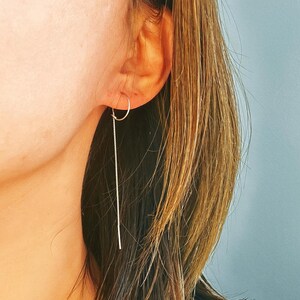 May include: A silver chain earring with a small hoop at the top. The earring is hanging from the earlobe of a person with long brown hair.