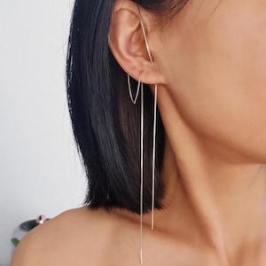 Könnte beinhalten: Silberne Ohrhänger mit filigranem Ketten-Design. Die Ohrringe werden getragen, wobei die Kette vom Ohr herabhängt. Die Ohrringe sind ein schlichtes, elegantes Accessoire.
