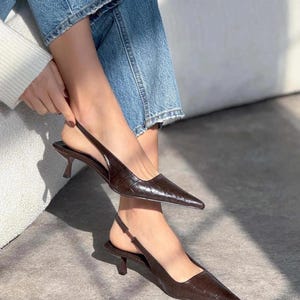 May include: Brown leather slingback heels with a pointed toe and a low heel. The shoes have a crocodile-embossed pattern.