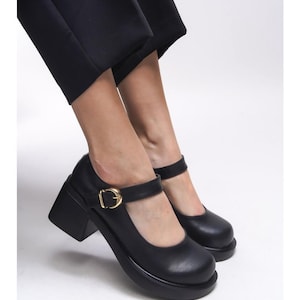 Peut inclure: Chaussures Mary Jane noires à plateforme avec un talon épais et une boucle dorée. Les chaussures ont un bout arrondi et une bride qui se ferme sur le dessus du pied. Le talon plateforme mesure environ 7,6 cm.