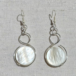 May include: A pair of silver earrings with a white mother-of-pearl disc pendant on each earring.