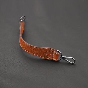 May include: A brown leather strap with a silver metal hook. The strap is stitched with white thread and has a slight curve.