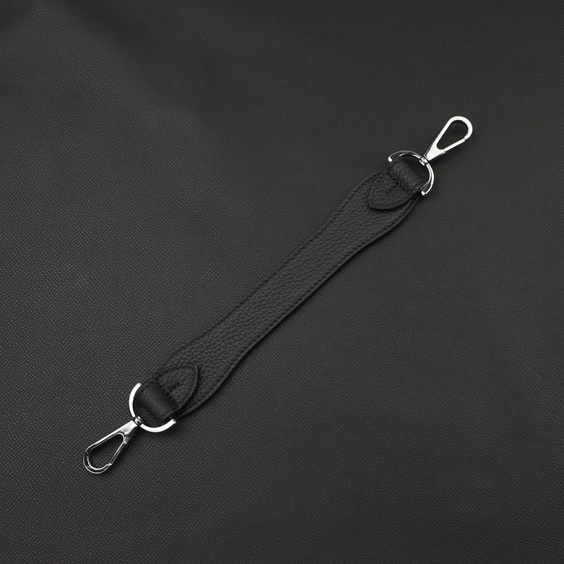 May include: A black leather strap with silver metal clasps. The strap is about 15 inches long.