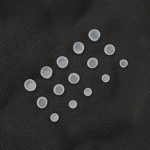 May include: A collection of 15 white plastic ink cups of various sizes, arranged in a triangular pattern on a black leather surface.