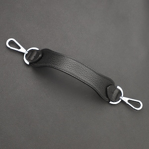 May include: A black leather handle with silver metal clasps. The handle is designed for a bag or purse.
