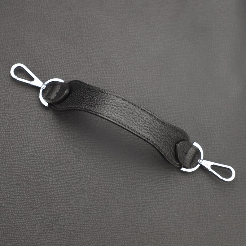 May include: A black leather handle with silver metal clasps. The handle is designed for a bag or purse.