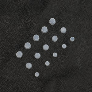 May include: A collection of white silicone bottle stoppers of various sizes arranged in a triangular pattern on a black textured surface.