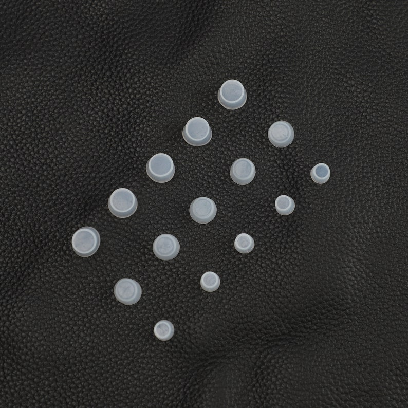 May include: A collection of white silicone bottle stoppers of various sizes arranged in a triangular pattern on a black textured surface.