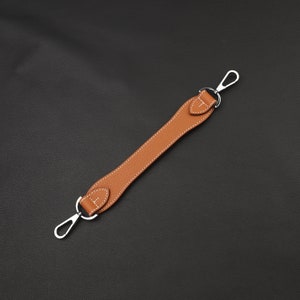 May include: A brown leather strap with two silver hooks. The strap is stitched with white thread.