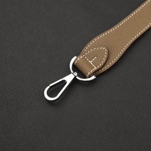 May include: Close-up of a brown leather strap with white stitching attached to a silver metal hook.
