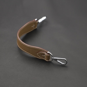 May include: A brown leather strap with a silver hook on one end and a silver loop on the other end.