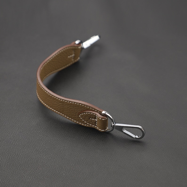 May include: A brown leather strap with a silver hook on one end and a silver loop on the other end.