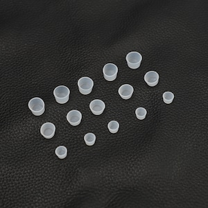 May include: A collection of 15 small, clear plastic cups of varying sizes, arranged in a semi-circle pattern on a black surface.