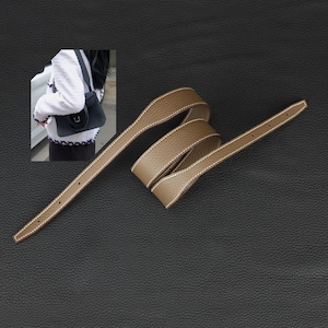 May include: A brown leather strap with white stitching. The strap is folded and coiled on a black surface.