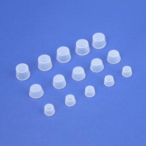 May include: Assortment of clear plastic bottle stoppers in various sizes. The stoppers are arranged on a blue background.