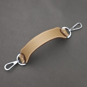 May include: A tan leather handle with silver metal loops on each end. The handle is stitched with white thread.