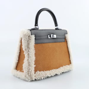 Könnte beinhalten: Eine braune und schwarze Handtasche mit schwarzem Griff und silberfarbener Hardware. Die Tasche hat einen braunen Wildleder-Körper, einen schwarzen Lederaufsatz und ist mit flauschigem, cremefarbenem Shearling verziert.