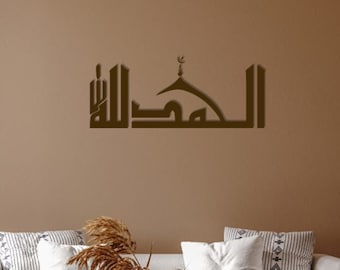 May include: A brown wooden wall decor with Arabic calligraphy and a mosque design. The decor is hanging on a brown wall in a living room setting with a white couch, a coffee table, and a wicker chair.