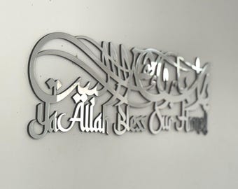 May include: A silver-colored wall art piece with Arabic calligraphy. The text reads "Ya Allah Bless Our Time" in a stylized script. The artwork is mounted on a white wall, creating a contrast.