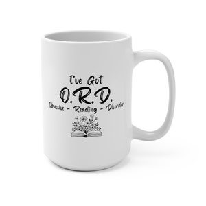 May include: White ceramic mug with the text "I've Got O.R.D. Obsessive - Reading - Disorder" in black script. A floral design is below the text. The mug has a large handle and is suitable for hot beverages.