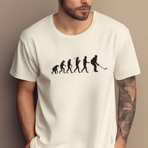 K&ouml;nnte beinhalten: Wei&szlig;es T-Shirt mit einer schwarzen Grafik der Evolution des Menschen, die mit einem Hockeyspieler endet, der einen Schl&auml;ger h&auml;lt.