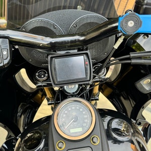 May include: Close-up of a black motorcycle with a gold-trimmed speedometer, a black windshield, and two black speakers mounted on the handlebars.