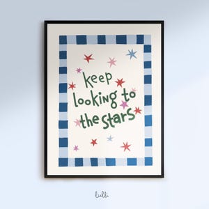 Pode incluir: Uma impressão de arte emoldurada com o texto "keep looking to the stars" em escrita verde. A impressão apresenta um fundo creme com estrelas vermelhas, rosa e azuis. Uma borda azul e azul claro quadriculada envolve o texto e as estrelas.