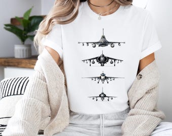 May include: A white short-sleeve t-shirt featuring a vertical graphic print of four different gray military fighter jets arranged in a column, each shown from a front-facing perspective with detailed wings, engines, and fuselage structures.