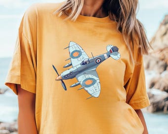 May include: Mustard-colored t-shirt featuring a detailed illustration of a vintage airplane. The graphic depicts a gray and blue aircraft with orange and blue circular accents. The shirt is a casual, short-sleeved style.