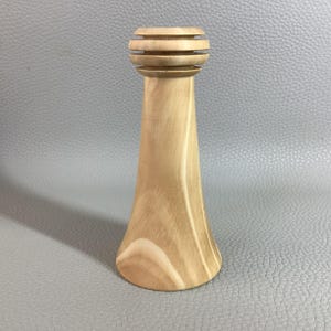 May include: A light-coloured wooden candlestick holder with a flared base and a cylindrical top with horizontal grooves. The wood grain is visible, designed to hold a single candle.
