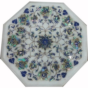 May include: Octagonal white marble table with inlaid floral design. The table features a central starburst and surrounding flowers in shades of blue and iridescent shell accents. A decorative piece for home decor.