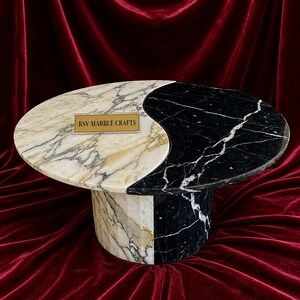 Könnte beinhalten: Ein Couchtisch aus Marmor mit Yin-Yang-Design. Eine Hälfte ist weiß und goldfarben, die andere ist schwarz mit weißen Adern. Der Sockel ist aus passendem Marmor. Der Text "RSV MARBLE CRAFTS" befindet sich auf einem goldenen Schild.