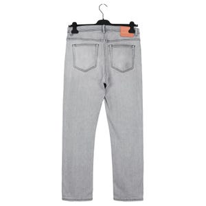 May include: Light gray denim jeans with a classic five-pocket design, hanging on a black hanger. The jeans feature a straight leg cut and a small, rectangular leather patch on the back waistband. The stitching is a darker gray.
