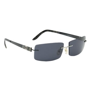 May include: Rimless sunglasses with dark gray lenses and black frames. The temples feature a silver and black design with a circular logo. The sunglasses have a sleek, modern design.