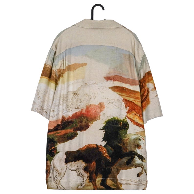 May include: A short-sleeved button-down shirt with a landscape and horse painting design. The shirt features a beige collar and a colorful illustration of horses and a mountain range. The artwork is in shades of brown, green, white, and orange.