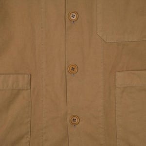 May include: Close-up of a tan-colored jacket with three visible buttons and two front pockets. The jacket has a classic design with a tailored fit, suitable for various occasions. The buttons are a matching tan color.