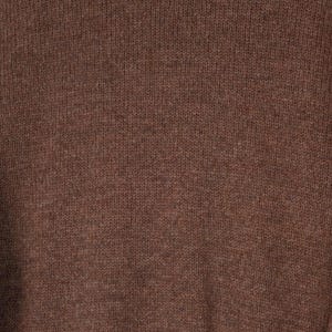 May include: Close-up of a brown knit fabric. The texture is visible, showing the individual stitches and the subtle variations in the yarn's color. The overall tone is a warm, earthy brown, suggesting a cozy garment or textile.