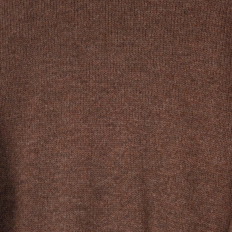 May include: Close-up of a brown knit fabric. The texture is visible, showing the individual stitches and the subtle variations in the yarn's color. The overall tone is a warm, earthy brown, suggesting a cozy garment or textile.
