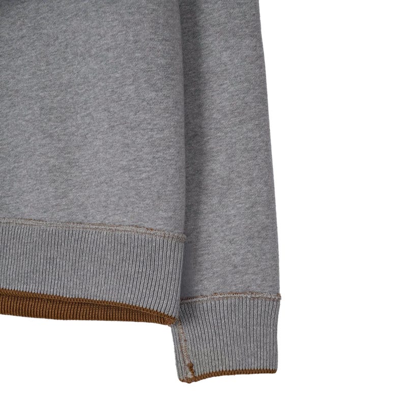 May include: Close-up of a grey sweatshirt sleeve. The ribbed cuffs and hem are a darker grey with a brown accent. The fabric appears to be a soft, comfortable material, suitable for casual wear.