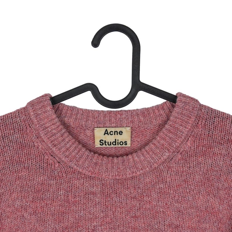 May include: A pink crew neck sweater with the "Acne Studios" label. The sweater is hanging on a black hanger. The knitwear has a textured appearance and a round neckline.