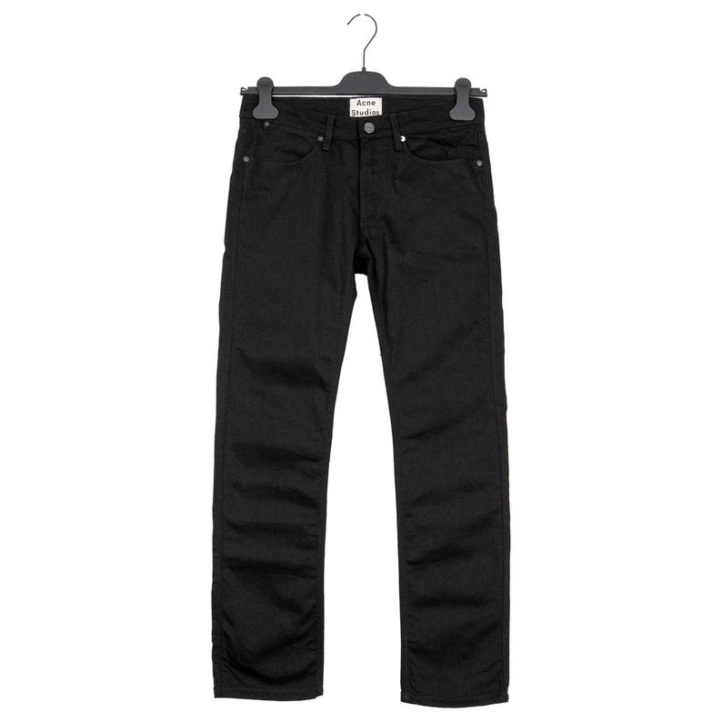 May include: Black denim jeans hanging on a black hanger. The jeans have a classic five-pocket design and a button and zipper closure. The brand name "Acne Studios" is visible on the hanger.