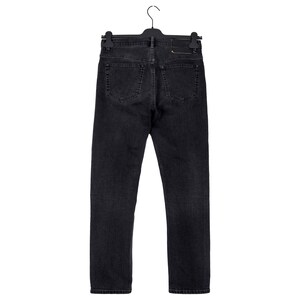 May include: Black denim jeans hanging on a black hanger. The jeans have a classic five-pocket design, with a dark wash and a leather patch on the back. The jeans are straight-legged and appear to be a medium weight.