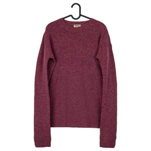 May include: A burgundy crew neck sweater with long sleeves, hanging on a black hanger. The sweater has a small label near the neckline. The fabric appears to be a soft knit.